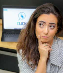 Autoimune: Sabrina Malichésqui pensativa com um computador atrás e a logo da sua empresa Click Solucoes Adm